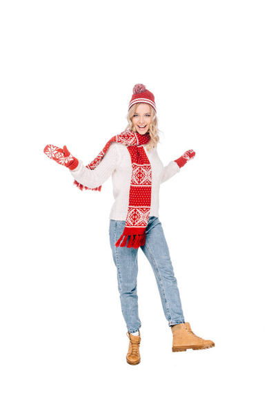 Вид в полный рост счастливой молодой женщины в красной шляпе, шарфе и с улыбкой на камеру, изолированной на белом
 - Фото, изображение