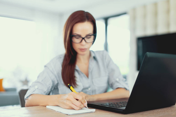 Jovem empreendedor freelancer escrevendo notas no laptop, dentro de casa
 - Foto, Imagem