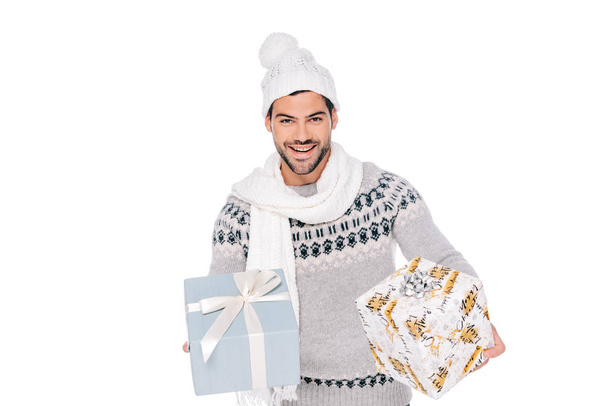 beau jeune homme heureux en pull, écharpe et chapeau tenant des boîtes-cadeaux et souriant à la caméra isolé sur blanc
 - Photo, image
