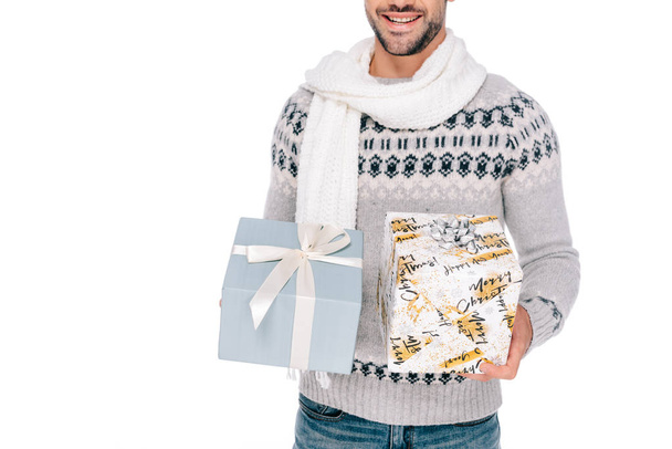 abgeschnittene Aufnahme eines lächelnden jungen Mannes in Pullover und Schal, der Geschenkboxen isoliert auf Weiß hält - Foto, Bild
