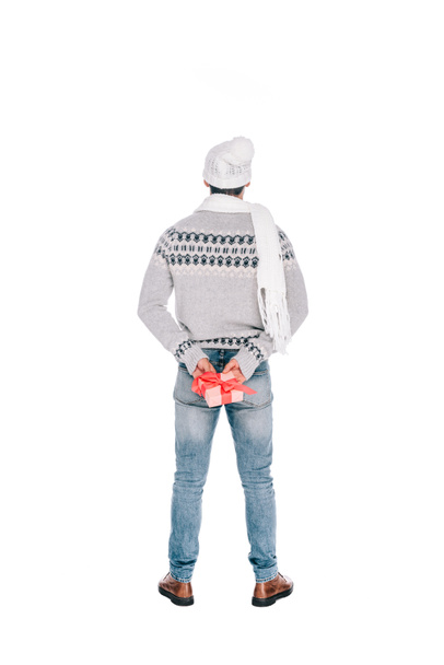 vista trasera del joven en suéter, bufanda y sombrero sosteniendo caja de regalo aislada en blanco
  - Foto, imagen