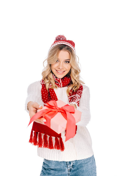 beautiful young woman in scarf and hat holding gift box and smiling at camera isolated on white  - Fotografie, Obrázek