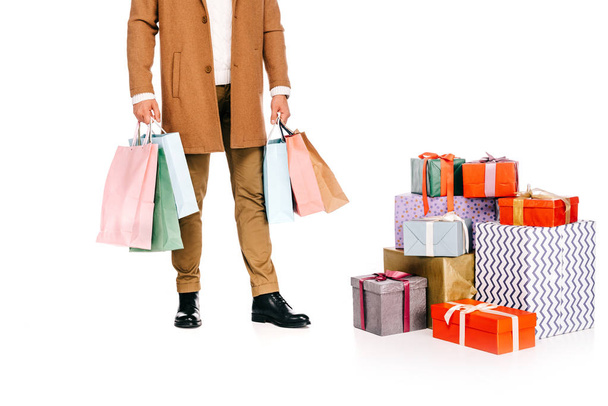recortado tiro de hombre sosteniendo bolsas de compras y de pie cerca de cajas de regalo aislado en blanco
 - Foto, imagen