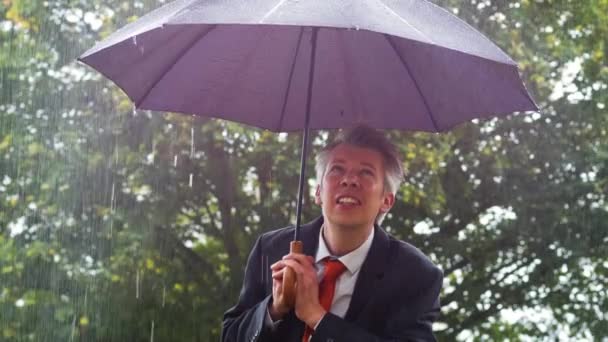 Caucasian businessman sheltering under an umbrella in the torrential rain - Πλάνα, βίντεο