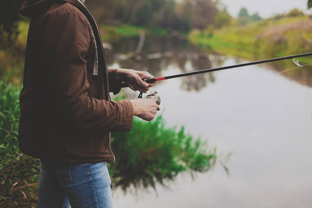 Young fisherman is fishing in river with spinning. Hobby and outdoor activities concept - Foto, Bild