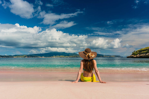 Молодая женщина, сидящая на песке в розовом пляже на острове Комодо
 - Фото, изображение