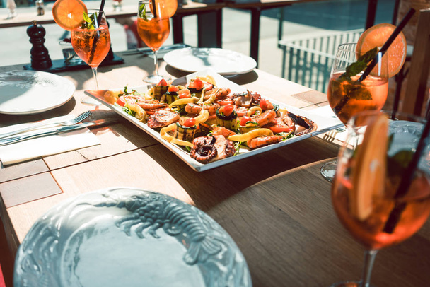 新鮮な魚介類のトレンディなレストランのテーブルの上のオレンジ色のカクテルを添えて - 写真・画像