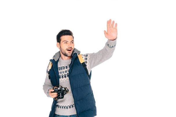 smiling young man with backpack holding camera and waving hand isolated on white - 写真・画像