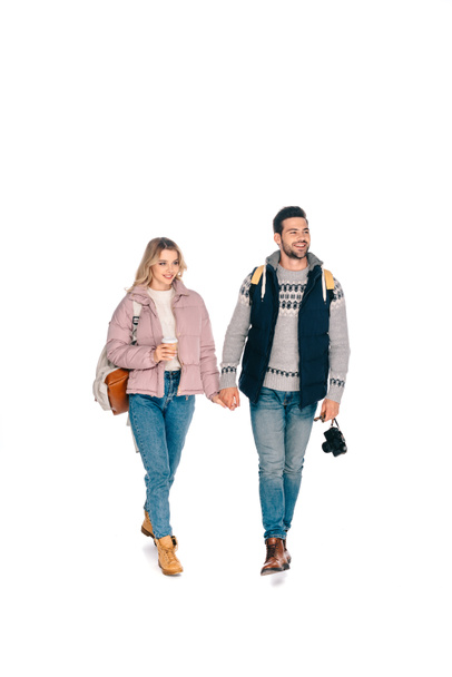full length view of smiling young couple of tourists with backpacks holding camera and coffee to go isolated on white - Fotoğraf, Görsel