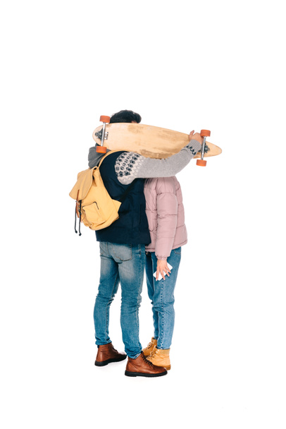full length view of young couple hiding faces behind longboard isolated on white - Fotoğraf, Görsel