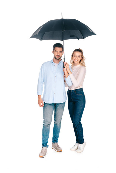 vista completa de la hermosa feliz pareja joven sosteniendo paraguas y sonriendo a la cámara aislada en blanco
 - Foto, Imagen