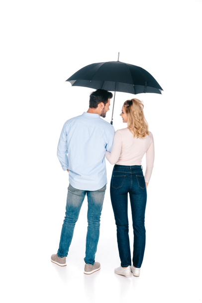 rear view of young couple holding umbrella and smiling each other isolated on white  - Foto, afbeelding