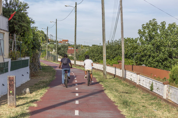 Deux garçons faisant du vélo sur une piste cyclable piétonne, ciel bleu comme arrière-plan et végétation, à Viseu, Portugal
 - Photo, image
