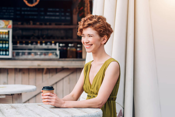 Happy redhead woman drinking coffee outdoor. The lifestyle, the emotions, the joy and youthfulness of the concept - Photo, image