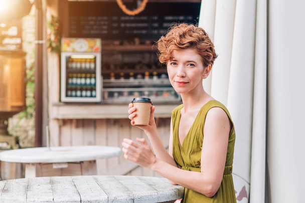 A beautiful redhead woman in a dress with cup of coffee. - Фото, изображение