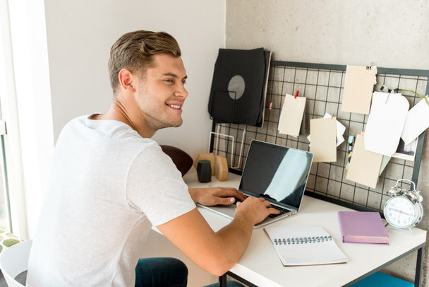 young smiling man using laptop at table at home office - Foto, immagini
