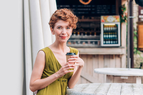 A beautiful redhead woman in a dress holding a cup of coffee. and looking at the camera, close up - Foto, imagen