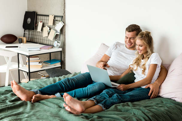 улыбающаяся молодая пара с цифровым ноутбуком, лежащая на кровати дома
 - Фото, изображение