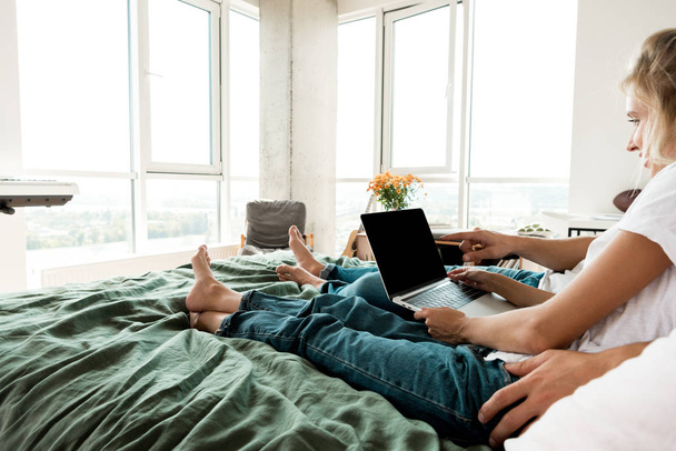 partial view of couple with digital laptop with blank screen resting on bed at home - Photo, Image