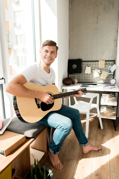 young smiling man playing acoustic guitar at home - Photo, Image
