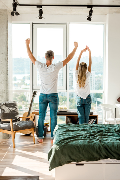 back view of young couple stretching while standing at window - Foto, afbeelding