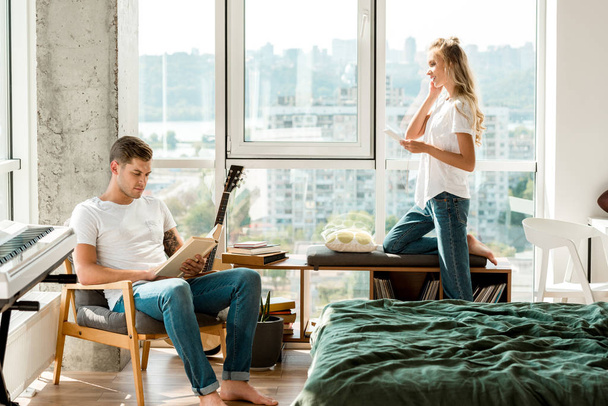 Nuori nainen kuulokkeet kuuntelee musiikkia, kun poikaystävä lukee kirjaa nojatuoli kotona
 - Valokuva, kuva