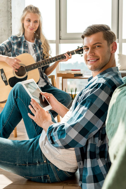 デジタル タブレットのアコースティック ギター、自宅でガール フレンドと笑みを浮かべて男 - 写真・画像