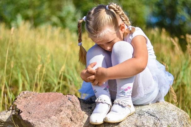 Una niña se pierde en la calle, se sienta en una roca y llora en un día soleado
 - Foto, Imagen