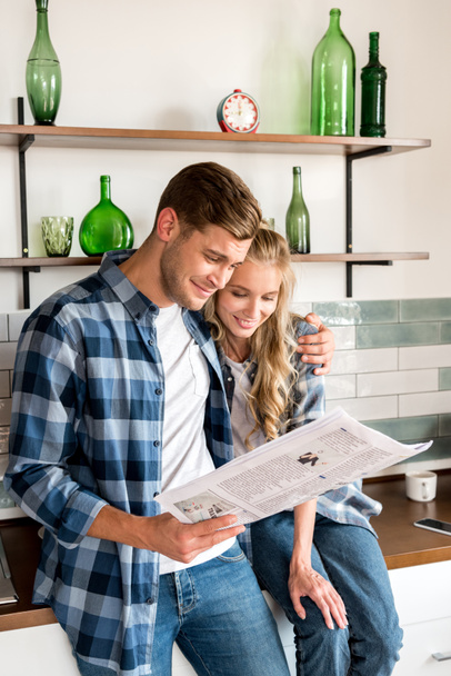 loving couple in casual clothing reading newspaper in kitchen at home - Photo, Image