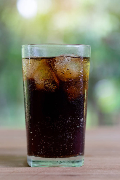 Refrescantes refrescos de refresco negro o cola con hielo en un vaso alto transparente con fondo natural
. - Foto, Imagen