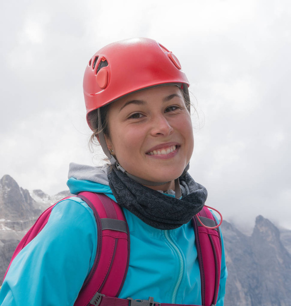 muotokuva nuori ja kaunis nainen vuorikiipeilijä sininen takki ja punainen kypärä hymyillen vuoristomaisema tausta
 - Valokuva, kuva