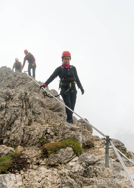 tres jóvenes y atractivos escaladores de montaña masculinos y femeninos en una empinada y expuesta Via Ferrata en Alta Badia en el Tirol del Sur en los Dolomitas italianos
 - Foto, imagen