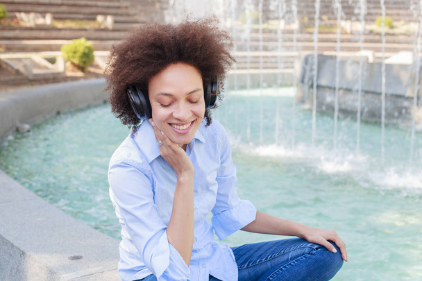 Portrait of Beautiful Happy Afro American Young Woman Listening Music with wireless headphones - Photo, Image