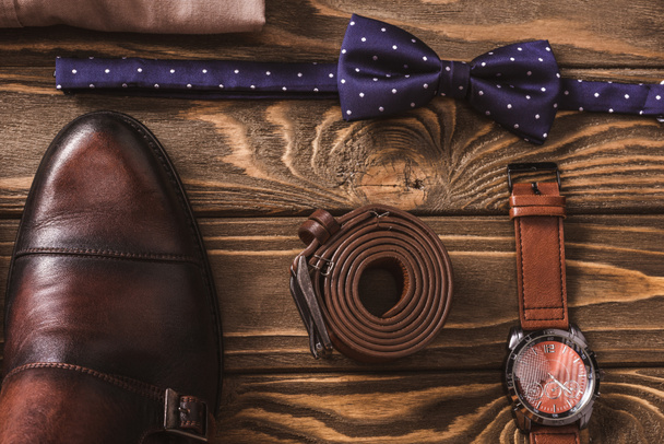 top view of leather male shoes, bow tie, belt and wristwatch arranged on wooden surface - Foto, Bild