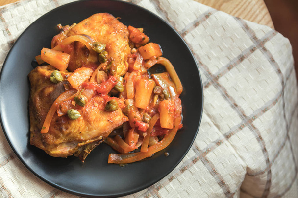 Heerlijk gebakken kip met groenten en kappertjes in zwarte schotel op tafel.  - Foto, afbeelding