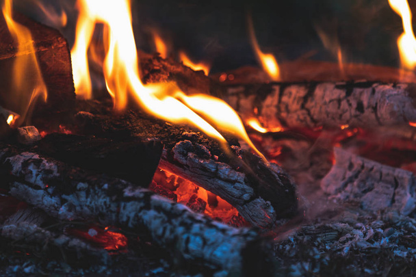 Charred wood in the fire. Burning wood in bright flames in the dark, close up. Toned dark fire background. - Photo, Image