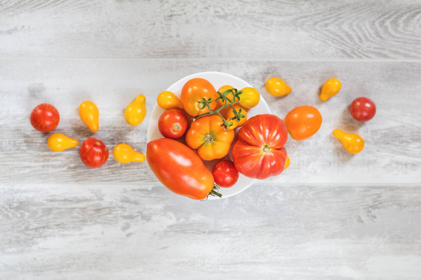 viele verschiedene rote orange gelbe Tomaten auf heller Holzoberfläche. schöne Lebensmittel Kunst Hintergrund, Ansicht von oben. - Foto, Bild