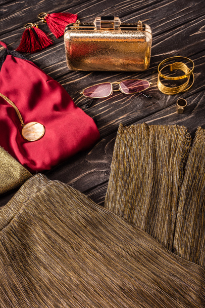 Nahaufnahme der Anordnung von goldenen und roten modischen femininen Accessoires und Kleidungsstücken auf Holzoberfläche - Foto, Bild