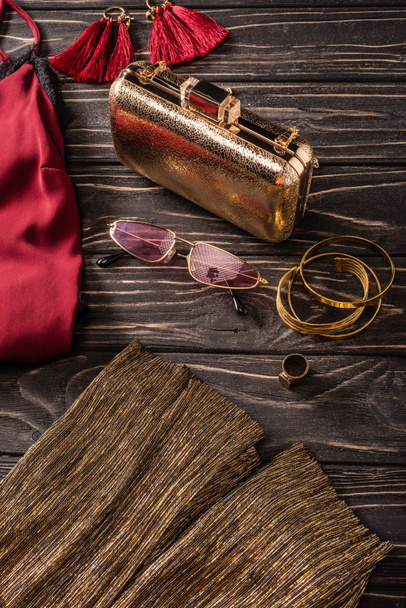 Nahsicht auf modische rot-goldene Damenhandtasche, Sonnenbrille und Schmuck auf Holztischplatte - Foto, Bild
