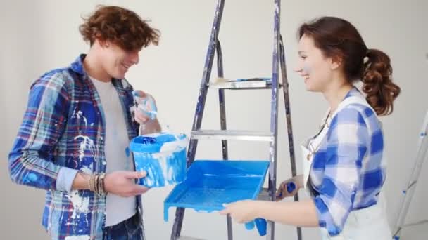 Έννοια της μετάβασης σε ένα νέο σπίτι. Νεαρό ζευγάρι ανακαινίζει και ζωγραφίζει τους τοίχους στο νέο σπίτι τους - Πλάνα, βίντεο