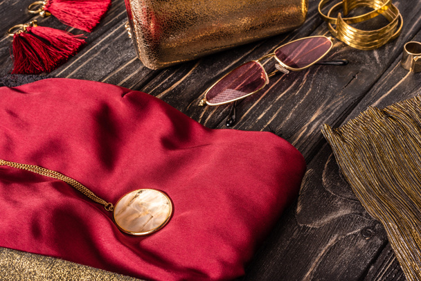 close up view of fashionable red and golden female purse, sunglasses and clothing on wooden tabletop - Photo, Image