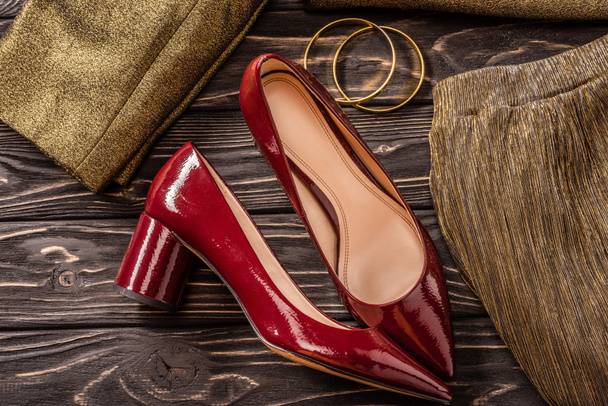 vista de perto da moda sapatos femininos vermelhos e dourados e pulseiras na mesa de madeira
 - Foto, Imagem