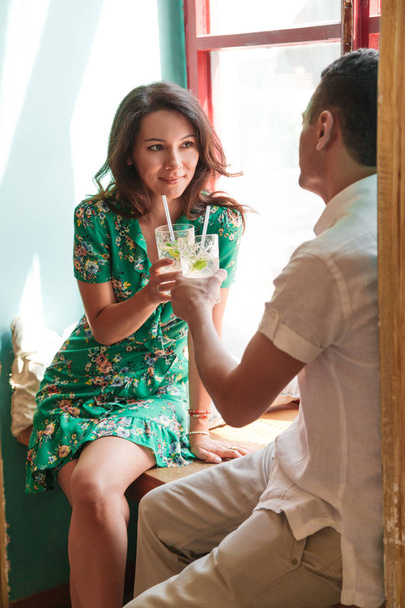 Beautiful couple sitting on the windowsill with coctails - Foto, afbeelding