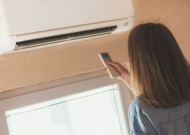 Woman holding remote control aimed at the air conditioner. - Photo, Image