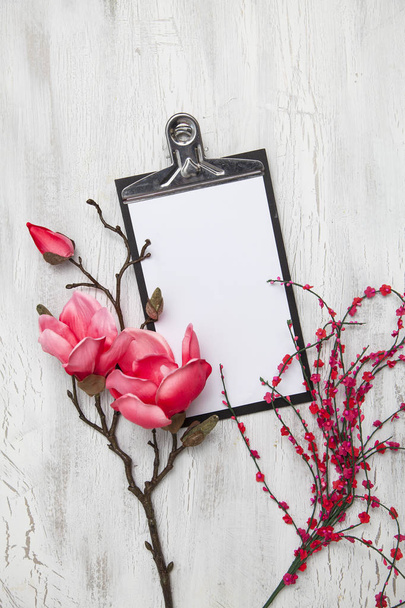 spring background with flowering branches and clipping board with white empty paper on wooden background, hello spring concept, top view   - 写真・画像