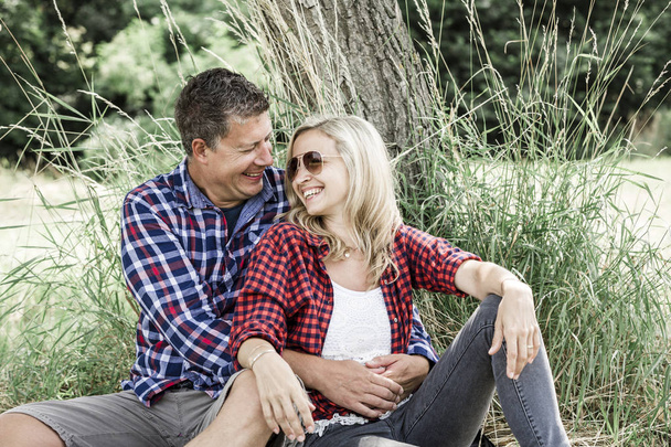 happy couple in love cuddling while sitting near tree in meadow  at sunny day  - Foto, Bild