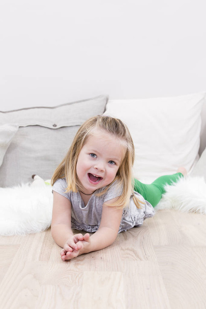 little cute girl having fun while lying on wooden floor near pillows  - Φωτογραφία, εικόνα