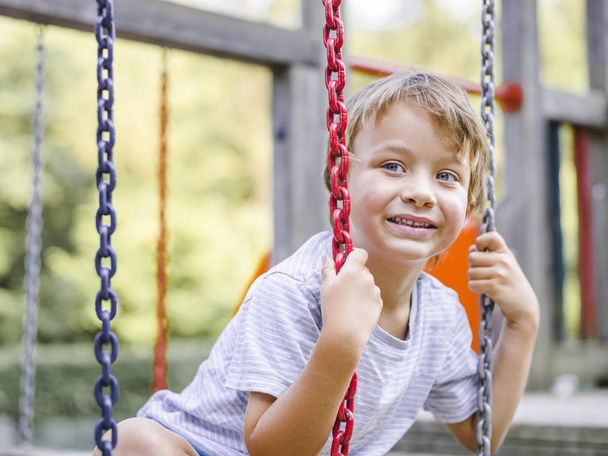 Blond boy having fun while playing on monkey swing at playground  - Foto, Bild
