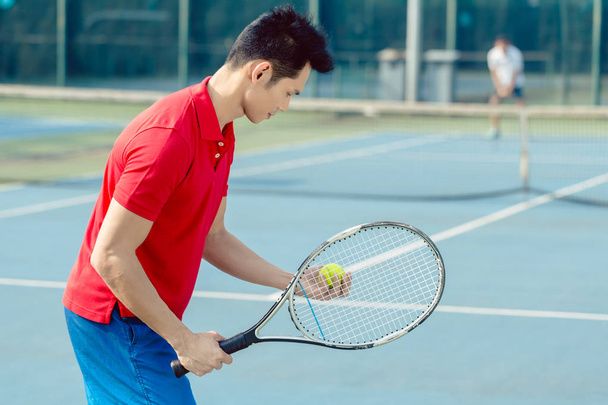 Asiático tenista olhando para a bola com concentração antes de servir
 - Foto, Imagem
