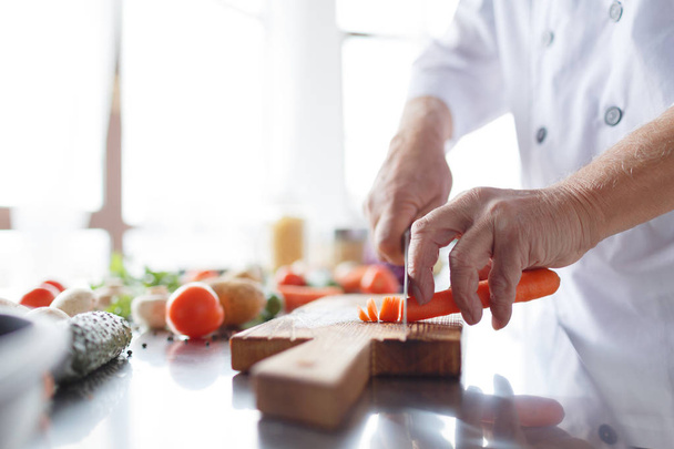 Male hands with a knife slicing carrots in the kitchen. A concept of cooking. Vegetables - Foto, Bild